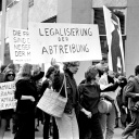 Historisches Schwarzweißfoto demonstrierender Frauen, von der eine ein Schild trägt mit der Aufschrift: "Legalisierung der Abtreibung".