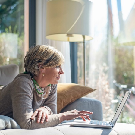 Eine Frau liegt auf dem Sofa vor ihrem Laptop während der Quarantäne