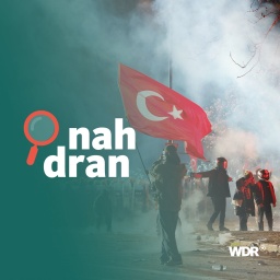 Mehrere Demonstranten stehen vor etlichen Polizisten. Tränengas-Rauch ist zu sehen. Ein Demonstrant schwenkt eine türkische Flagge. Im Vordergunrd ist das Logo des Podcasts nah dran zu sehen. 