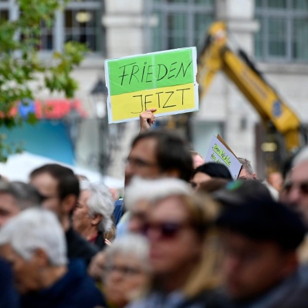 Ein Gegendemonstrant hält ein Schild hoch mit der Aufschrift 'Frieden jetzt' bei einer Kundgebung der Bayerischen SPD.  