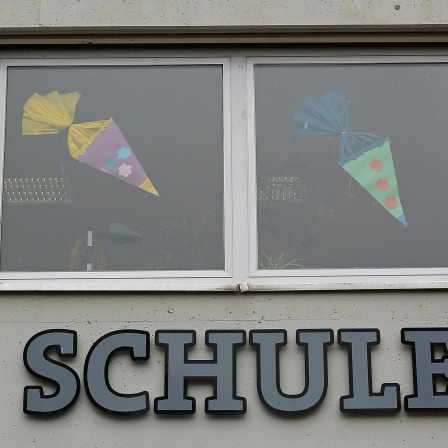 Gebastelte Schultüten kleben an alten Fenstern einer Schule