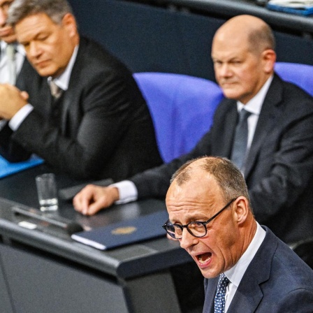 Merz (CDU) am Rednerpult im Bundestag. Dahinter Scholz (SPD) und Habeck (Grüne).