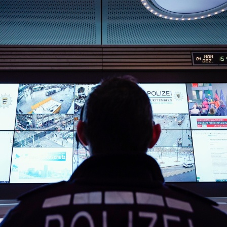 Ein Beamter steht im Führungs- und Lagezentrum des Polizeipräsidiums Mannheim vor einer Wand mit Bildschirmen