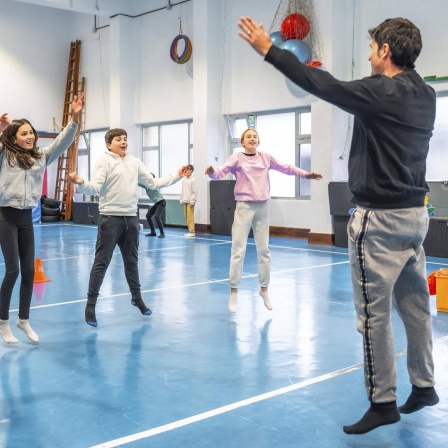 Symbolbild: Schüler machen zusammen mit ihrem Sportlehrer in der Schule Hampelmänner und Fitnessübungen.