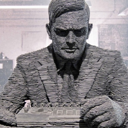 Skulptur des Computerpioniers Alan Turing vor einem alten Foto.