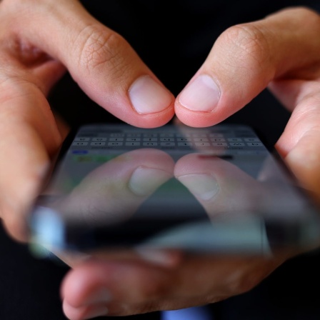 Ein Jugendlicher tippt eine WhatsApp-Nachricht auf seinem Smartphone.