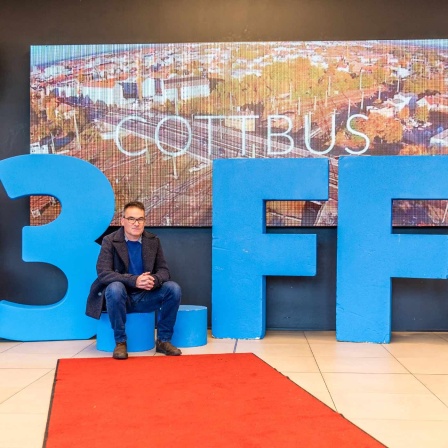 Bernd Buder, Programmdirektor des Filmfestivals Cottbus, sitzt in einem Einkaufszentrum vor dem aus Kunststoff gebildeten Schriftzug «33. FFC»