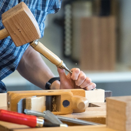 Ein Mann bearbeitet an einer Werkbank ein Holzteil.