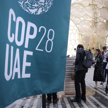 Besucher füllen Wasserflaschen neben einer Fahne mit der Aufschrift "COP28 UAE"