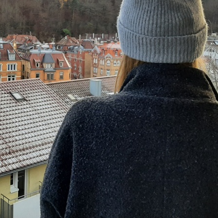 Annika steht mit dem Rücken zum Betrachter und schaut auf eine kleine Stadt