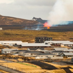 Vulkaneruption nahe der isländischen Stadt Grindavik am 1. April 2025. Im Vordergrund sind Gebäude der Stadt zu sehen, im Hintergrund hellorange Lava-Eruptionen in einer Vulkanspalte. 