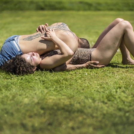 Ein Mann und eine Frau liegen während einer Massage-Workshops ineinander verschlungen auf einer Wiese.