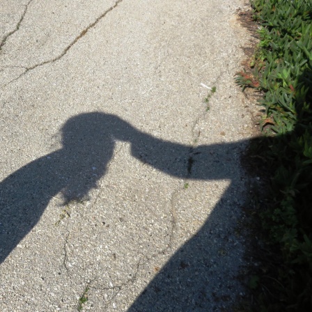 Der Schatten eines Kindes wird berührt von dem Schatten eines Erwachsenen.