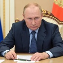 Wladimir Putin sitzt vor zwei Flaggen an einem Tisch.