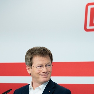 DB-Chef Richard Lutz am Mikrofon auf einer Pressekonferenz. Im Hintergrund das DB-Logo.