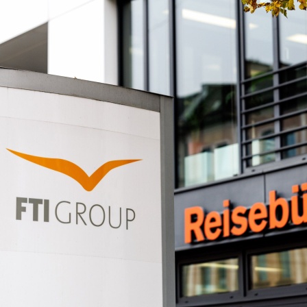 Der Schriftzug "FTI Group" ist auf einer Stele neben einem Reisebüro zu sehen.