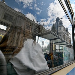 Eine Frau sitzt in einer historischen, blau-gelb gestrichenen Tram. Sie ist durch das Fenster nur von hinten zu sehen.