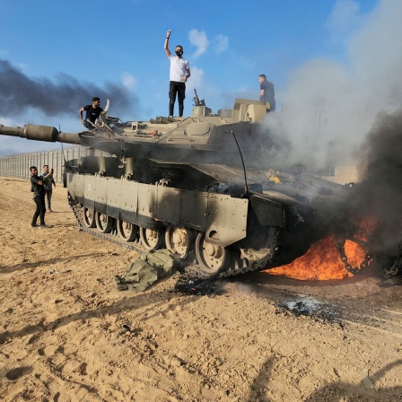 Palästinenser feiern an einem zerstörten israelischen Panzer am Zaun des Gazastreifens.