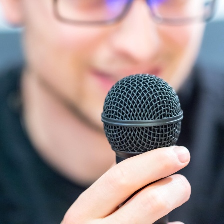 Junger Mann hält Mikrofon vor dem Gesicht: Wenn man in ein Mikrofon spricht, kommt beim Mikrofon der Schall nur über die Luftleitung an - nicht über die Knochenleitung. Deshalb klingt es so anders.
