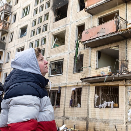 Eine alte Frau steht vor einer Ruine eines Mehrfamilienhauses in der Ukraine