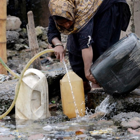Eine pakistanische Frau füllt Gefäße mit Trinkwasser an einem Brunnen.