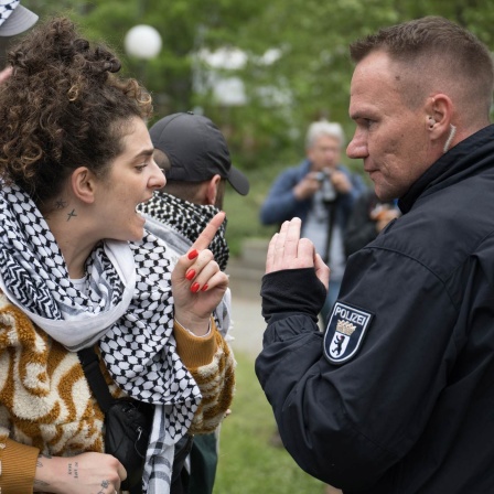 Eine Frau diskutiert während propalästinensischen Demonstration der Gruppe "Student Coalition Berlin" auf dem Theaterhof der Freien Universität Berlin mit einem Polizeibeamten (Bild:  Sebastian Christoph Gollnow/dpa)