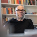 Der Soziologe Stephan Lessenich sitzt in einem schwarzen T-Shirt an seinem Schreibtisch vor einem Bücherregal.