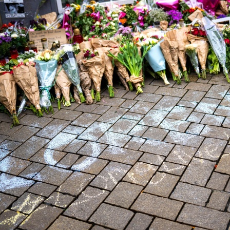 Vor einer Ansammlung von Blumen und Kerzen steht mit Kreide "Lorenz" in großen Buchstaben auf dem Pflasterstein.