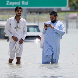 Zwei Männer gehen durch Hochwasser. Schwere Gewitter zogen am Dienstag über die Vereinigten Arabischen Emirate hinweg und brachten dem Wüstenstaat Dubai innerhalb weniger Stunden so viel Regen wie seit anderthalb Jahren nicht mehr, wodurch Teile der Hauptverkehrsstraßen und der internationale Flughafen überflutet wurden.