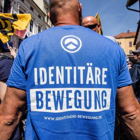 Ein Mann mit einem blauen Shirt, auf dem "Identitäre Bewegung" steht, steht auf einer Demonstration in Sachsen-Anhalt. (Bild: picture alliance / ZUMAPRESS / Sachelle Babbar) 