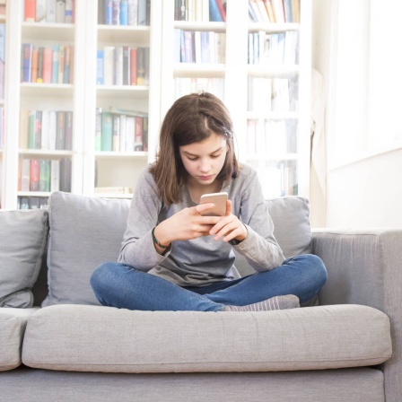 Mädchen sitzt mit Smartphone auf der Couch