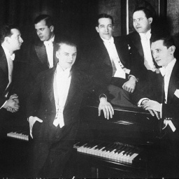 Alte schwarz-weiß Foto von den Comedian Harmonists. In schwarze Anzüge gekleidet haben sie sich um ein Klavier versammelt