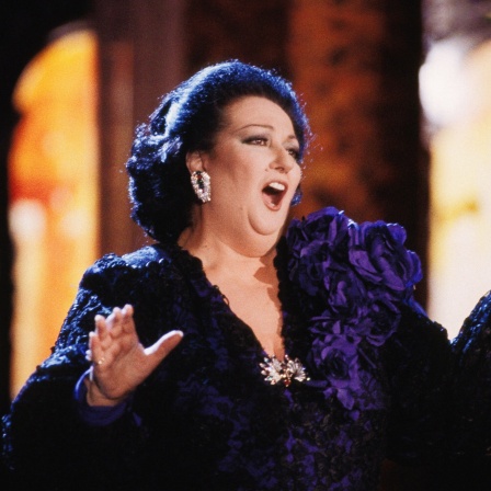 Eine dunkelhaarige Frau, Montserrat Caballé, singt in einem dunkelblauen Kleid