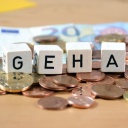 Das Wort Gehalt aus einzelnen Buchstaben auf Würfeln auf Euromünzen, im Hintergrund ein Geldschein.
