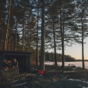 Eine kleine Hütte zwischen hohen Bäumen an einem winterlichen See.