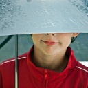 Ein junge in roter Sportjacke lächelt unter einem naßen Regenschirm hervor, seine Augen sind verdeckt