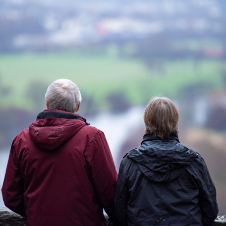 Ein Mann und eine Frau stehen auf einer Aussichtsplattform und schauen auf einen Fluss und eine Landschaft.
