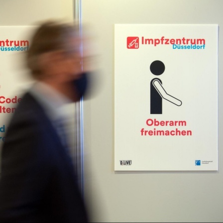 Szene aus dem Impfzentrum Düsseldorf. Ein Mann geht an einem Hinweisschild vorbei.