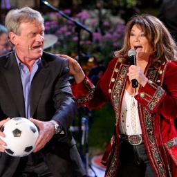 Sängerin Wencke Myhre und Fußballer Sepp Maier stehen gemeinsam auf einer Bühne. Sepp Maier hält einen Fußball in der Hand und Wencke Myhre ein Mikrofon.