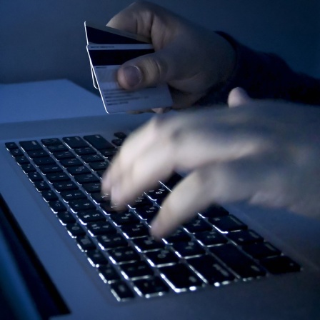 Ein Krimineller sitzt am Computer und hat EC-Karten in der Hand.