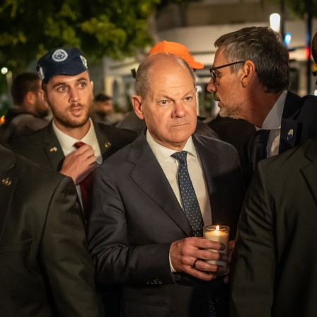 Bundeskanzler Olaf Scholz (SPD) steht, umringt von Bodyguards, bei seinem Solidaritätsbesuch in Israel mit einer Kerze in der Hand am Dizengoff Square im Zentrum von Tel Aviv.