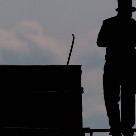 Ein Schornsteinfeger läuft mit seinem Kaminkehrerwerkzeug auf einem Dach entlang.