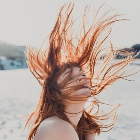 Junge Frau mit im Wind wehenden Haaren in einem verschneiten Feld stehend
