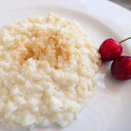 Milchreis mit Zimtzucker bestreut und zwei Kirschen garniert (Bild: picture alliance/Martina Raedlein)