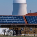 Wasserdampf steigt aus dem Kühlturm vom Atomkraftwerk Isar 2. Davor steht ein Stall mit einer Photovoltaikanlage.