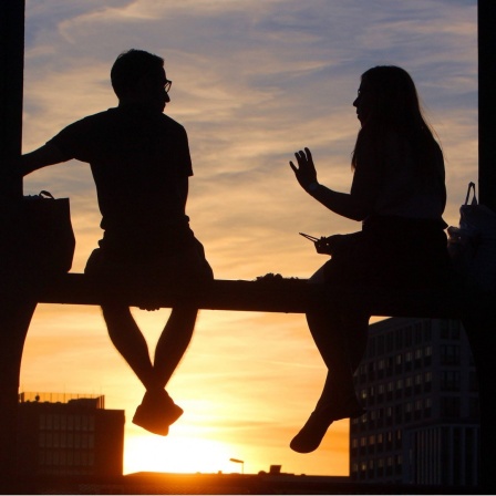Zwei Personen sitzen auf dem Geländer der Hackerbrücke in München und genießen den Sonnenuntergang bei einer Unterhaltung.