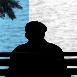 Das Beitragsbild des ARD Radiofeature "No Nation - Doku über Staatenlosigkeit" zeigt einen älteren Mann von hinten der auf einen See schaut. 