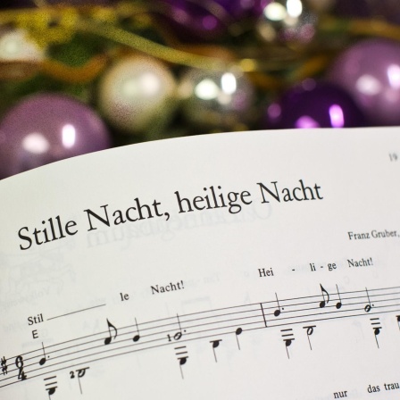 Noten zum Weihnachtslied «Stille Nacht, heilige Nacht», im Hintergrund Christbaumkugeln
