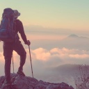 Ein Mensch mit Rucksack schaut von einem Gipfel in eine Berglandschaft