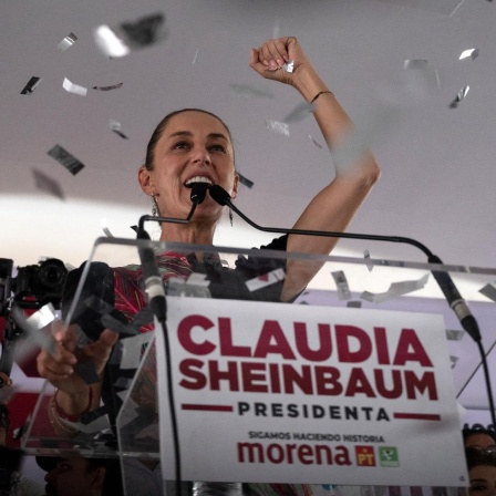 Claudia Sheinbaum steht auf einem Podium und reckt die rechte Faust in die Höhe, während Konfetti auf sie herabregnet.